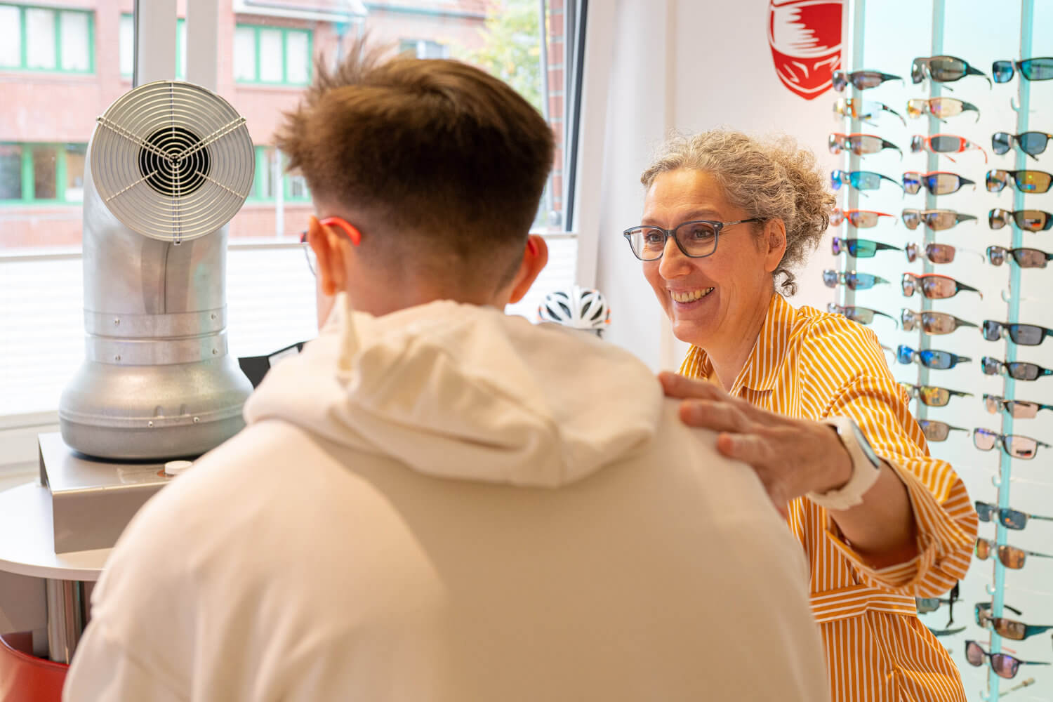 Eine Optikerin spricht mit einem jungen Kunden in einem Brillengeschäft.