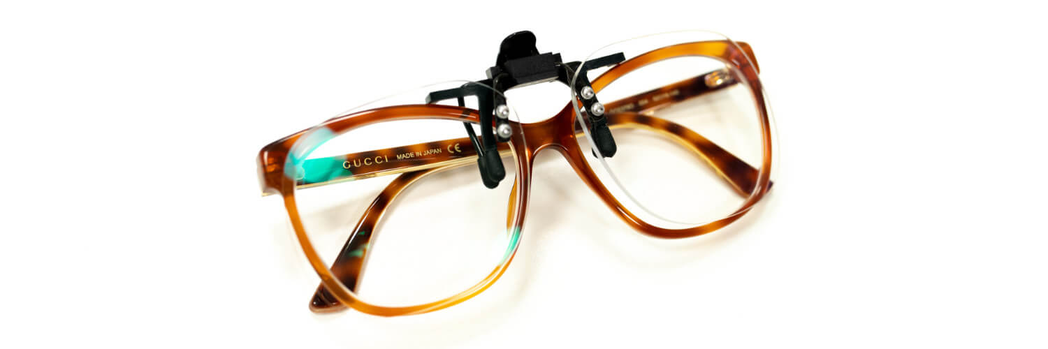 Braune Brille mit aufgesetztem schwarzem Clip und seitlichen Bügeln vor weißem Hintergrund