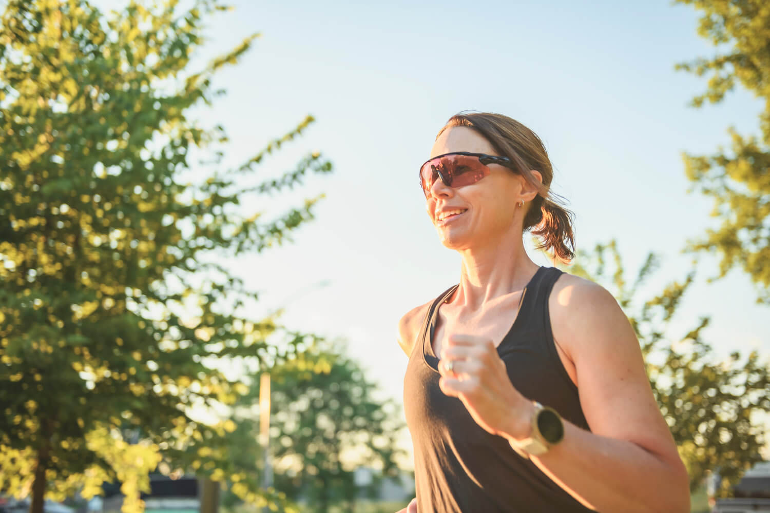 Läuferin mit Sportsonnenbrille joggt bei sonnigem Wetter im Freien.