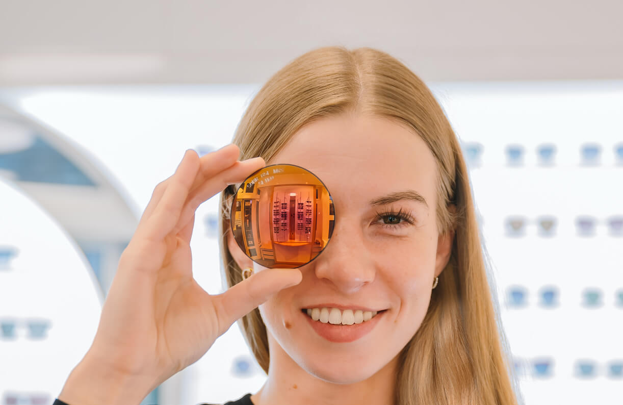 Lächelnde Frau hält ein Brillenglas vor ein Auge.