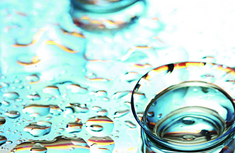 Kontaktlinse in einer Glasschale auf einer mit Wassertropfen bedeckten Oberfläche.